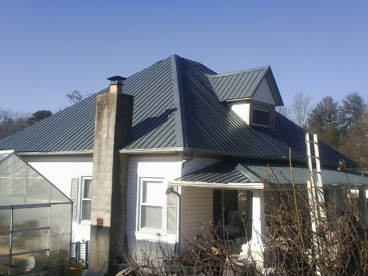 Dark blue standing seam metal roof on a white farmhouse with dormer — Slate & Tile Roof Repair by Roofing Brothers in Rosemary Beach