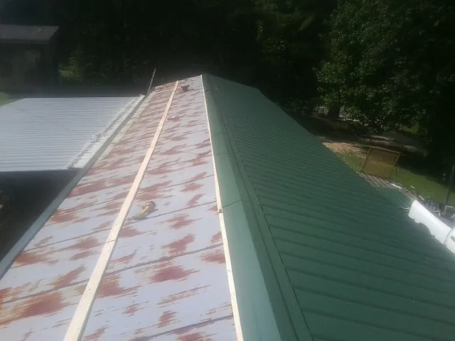 Old rusted panels beside newly installed green metal roofing — Wind Damage Roof Repair by Roofing Brothers in Rosemary Beach